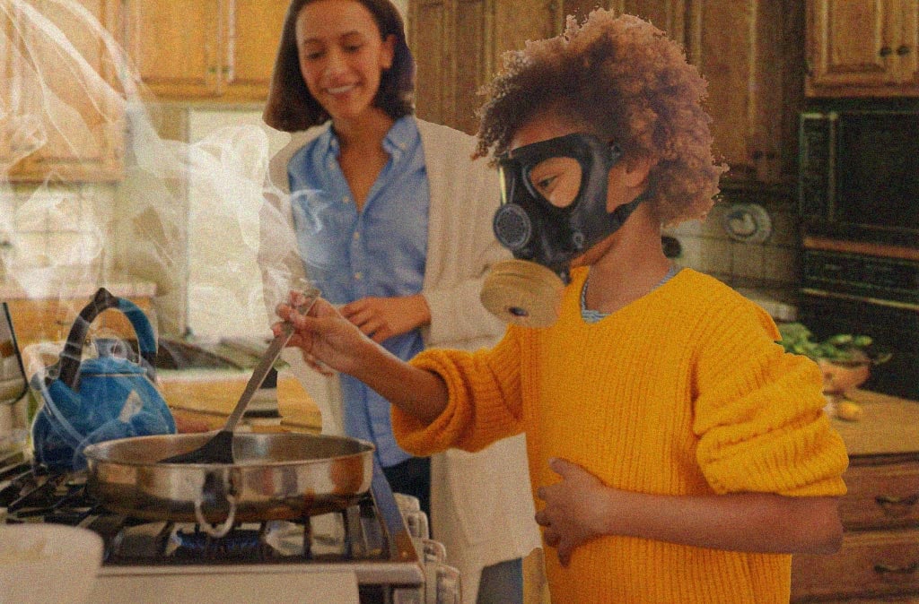 A mom and kid cooking in the kitchen with the kid at the stove, wearing a gas mask