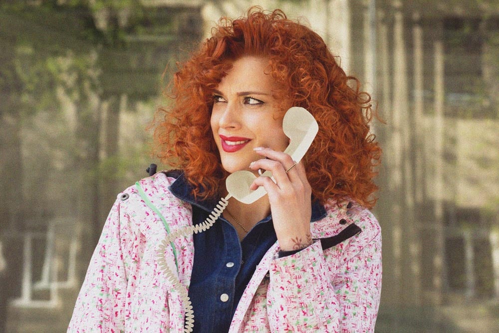 A red headed woman on a corded phone looking to the left